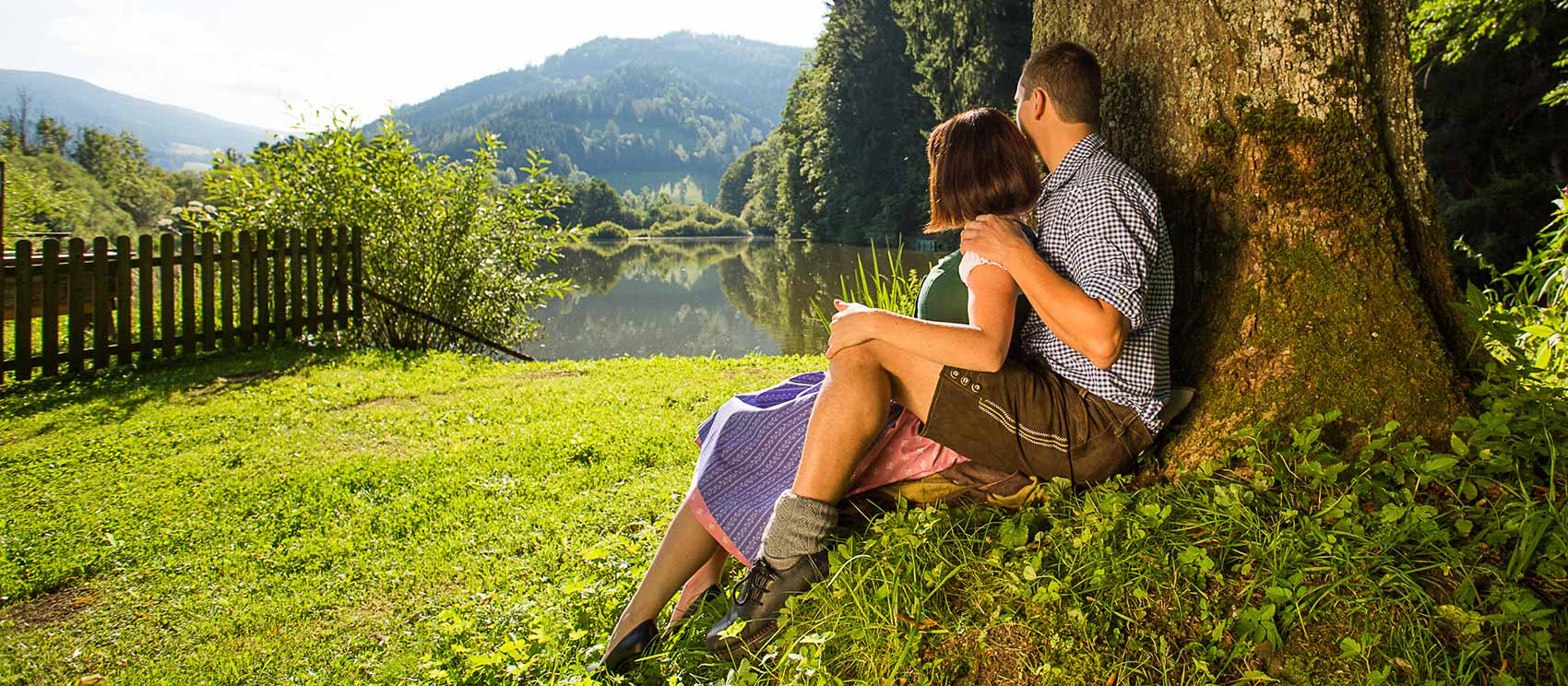 Pärchen sitzt an einem Baum und schaut auf den Teich.