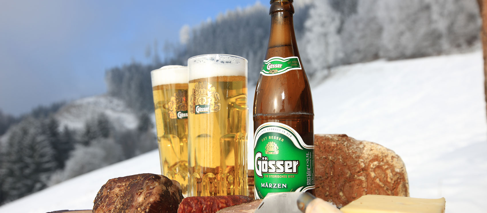 Steirische Jause mit Bier, Brot, Geselchtes und Würste - im Hintergrund Schneelandschaft